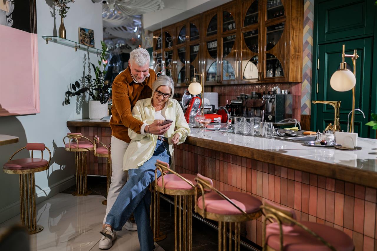 Two customers looking at a phone together at the counter of a cafe.